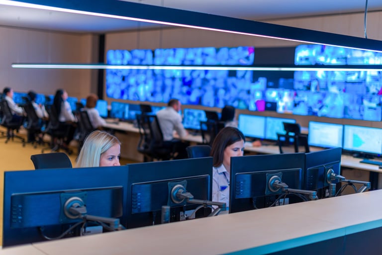 Modern control room with staff at computer workstations and large display screens showing data and monitoring feeds