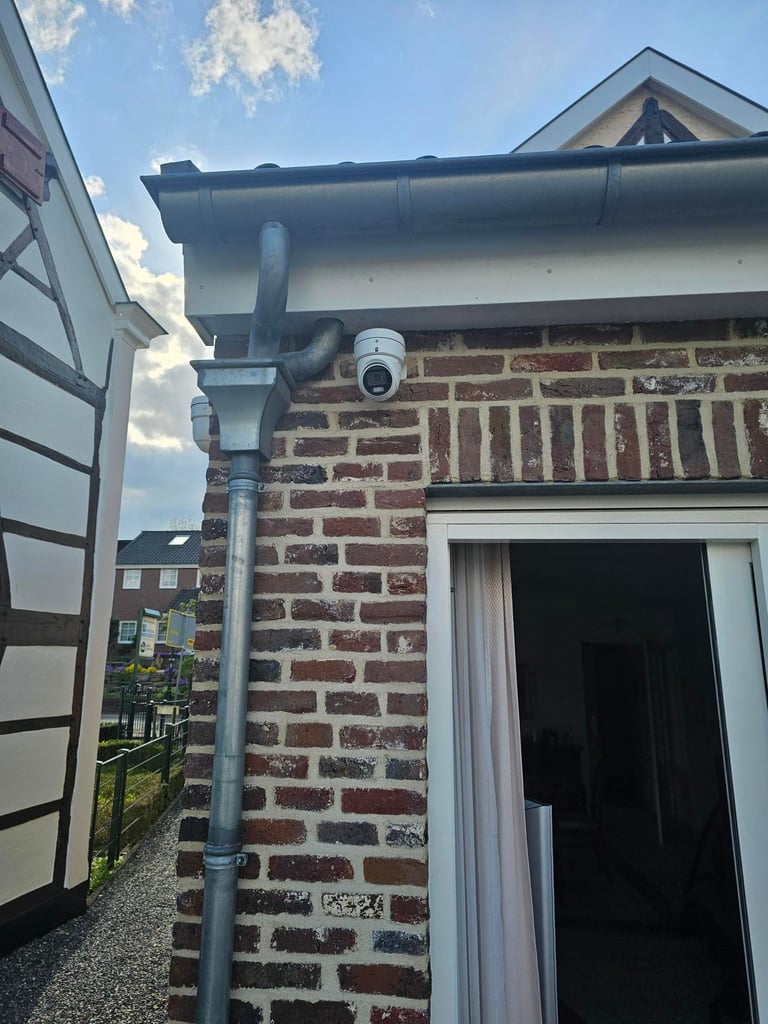 Security camera mounted on brick building exterior with downspout and gutter system visible